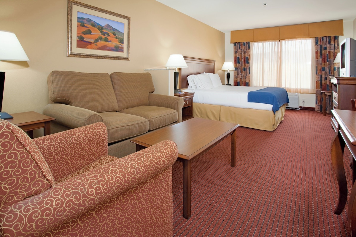A hotel room with a bed, two sofas, a table, and a painting on the wall.