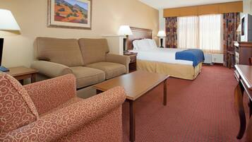 A hotel room with a bed, two sofas, a table, and a painting on the wall.