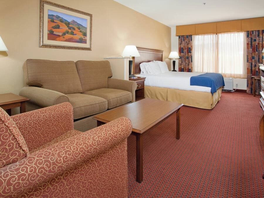 A hotel room with a bed, two sofas, a table, and a painting on the wall.