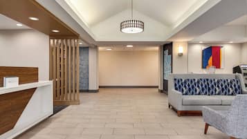 A hotel reception area with a wooden reception desk, a grey sofa, and a colorful abstract painting on the wall.