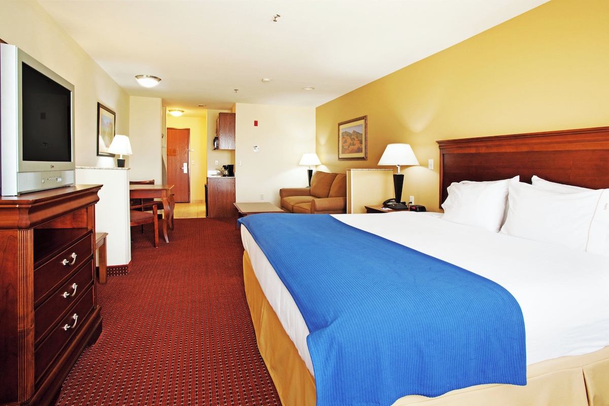 A hotel room with a bed, a desk, a chair, a television, and a lamp.