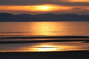 Un atardecer sobre una masa de agua tranquila con montañas a lo lejos.