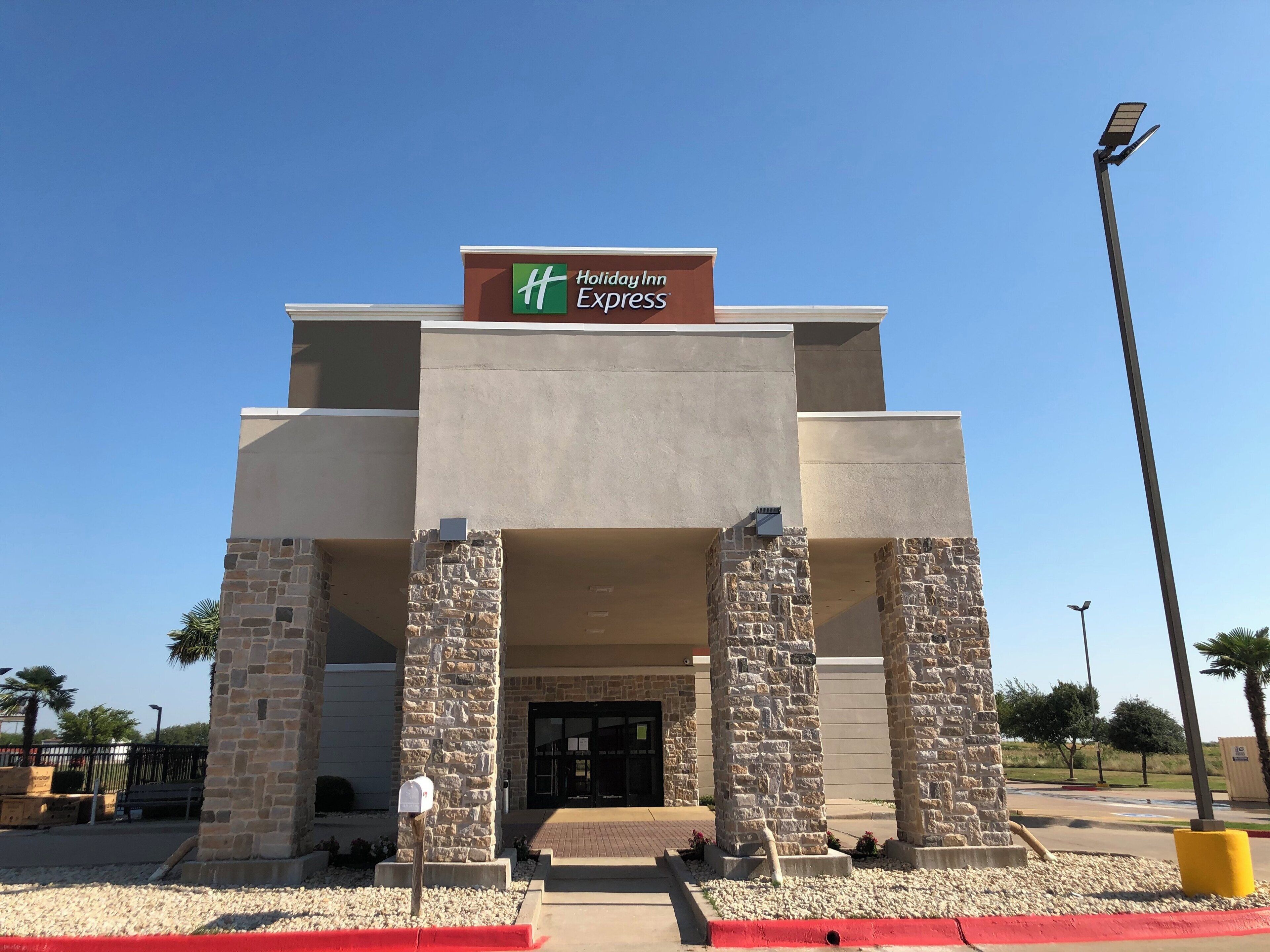 A Holiday Inn Express building with a stone facade, a prominent sign, and a clear sky.