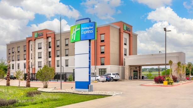 A Holiday Inn Express hotel with a modern design, featuring a large sign, multiple parking spaces, and a landscaped entrance area. - Holiday Inn Express : Hillsboro I-35 by IHG (Hillsboro)