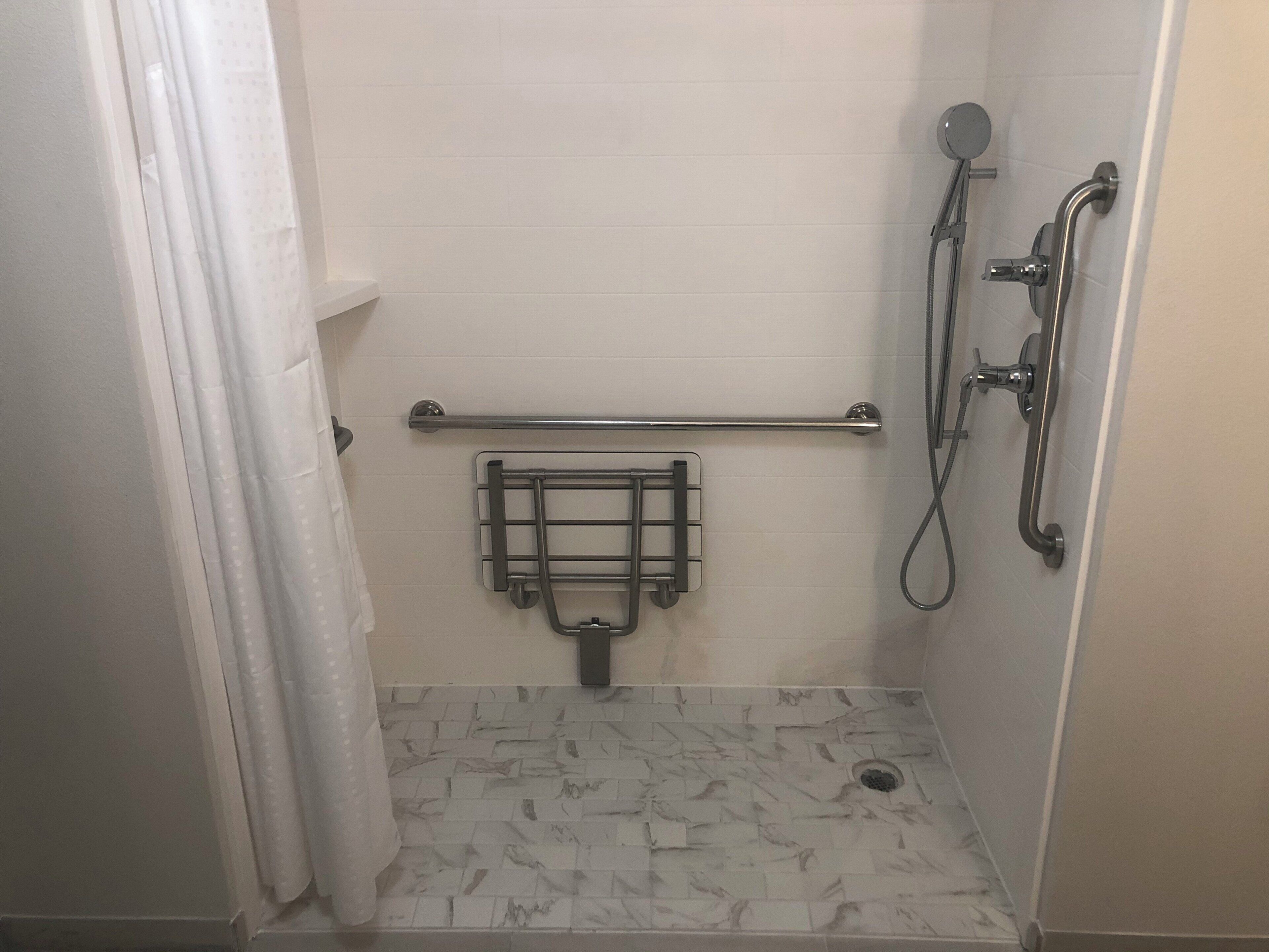 A shower area with a grab bar, a handheld showerhead, and a floor drain.
