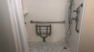 A shower area with a grab bar, a handheld showerhead, and a floor drain.