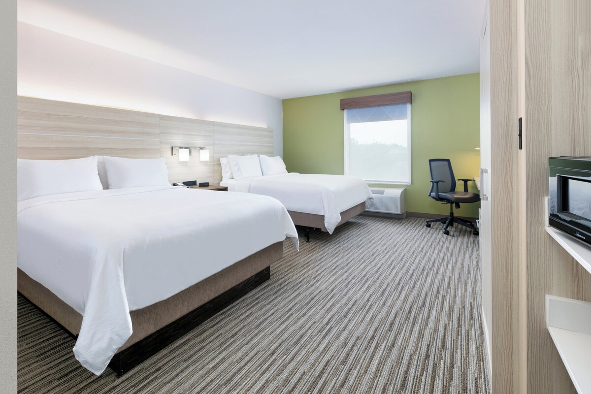 Quarto de hotel com duas camas, uma escrivaninha, uma cadeira, uma TV e uma janela.