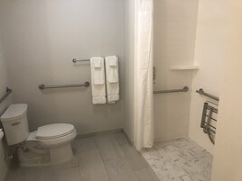 Un baño con inodoro, cortina de ducha y barras de apoyo.
