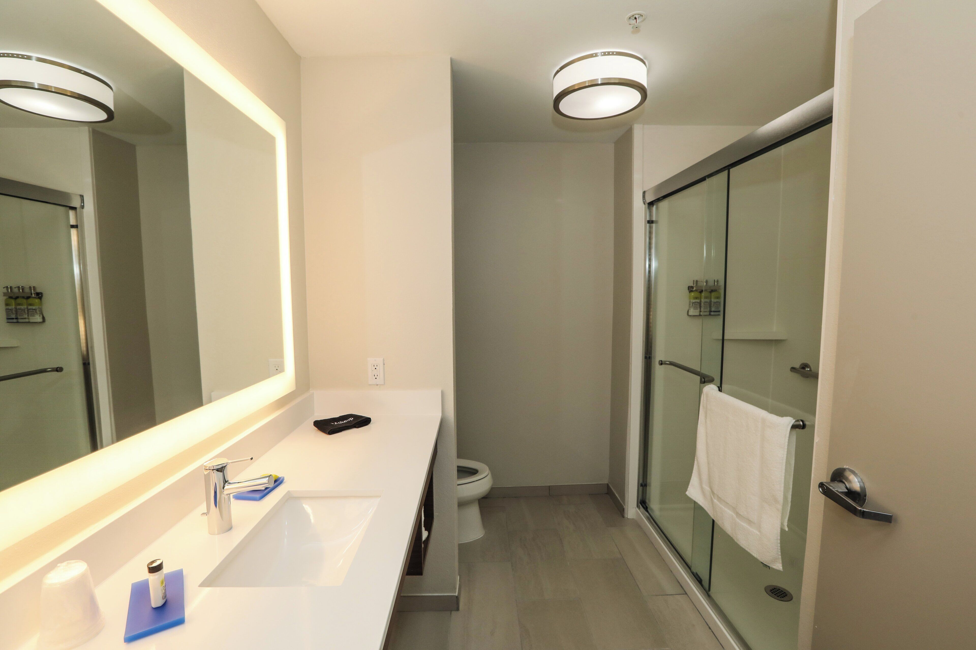 Un baño moderno con un espejo grande, un lavamanos, una ducha y un inodoro.
