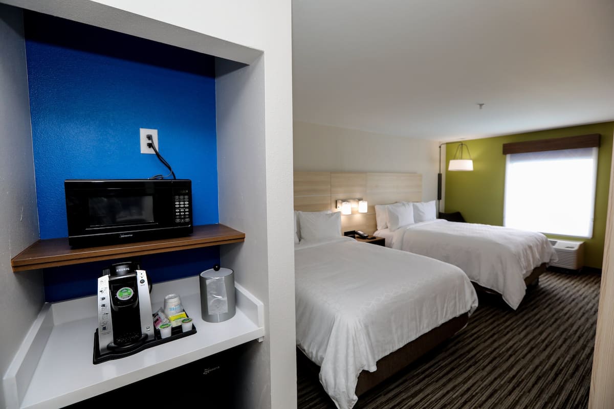 Quarto de hotel com micro-ondas numa prateleira, máquina de café e duas camas com roupa de cama branca.