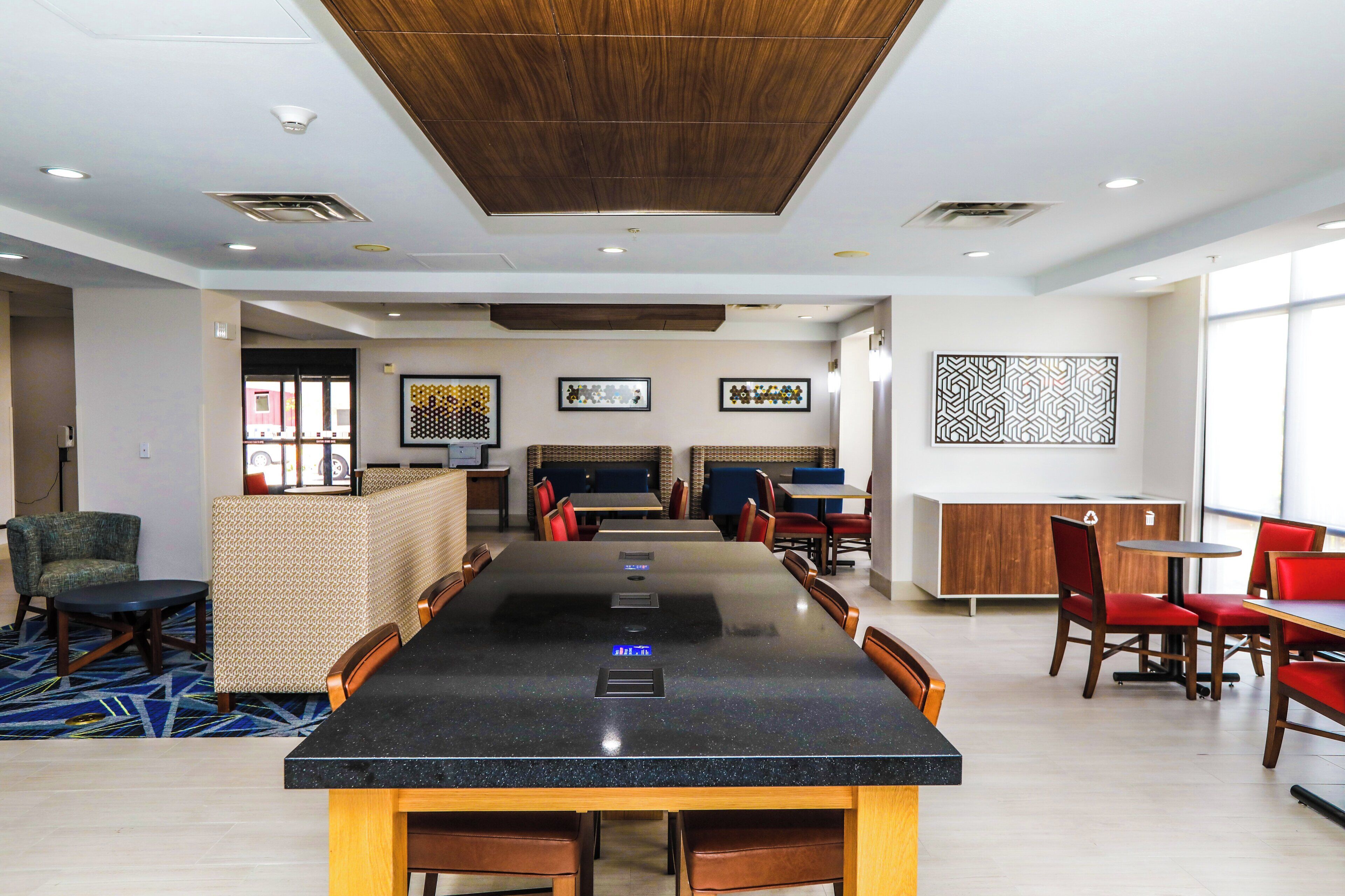 Un hall de hotel con una larga mesa común, disposiciones para sentarse y obras de arte en las paredes.