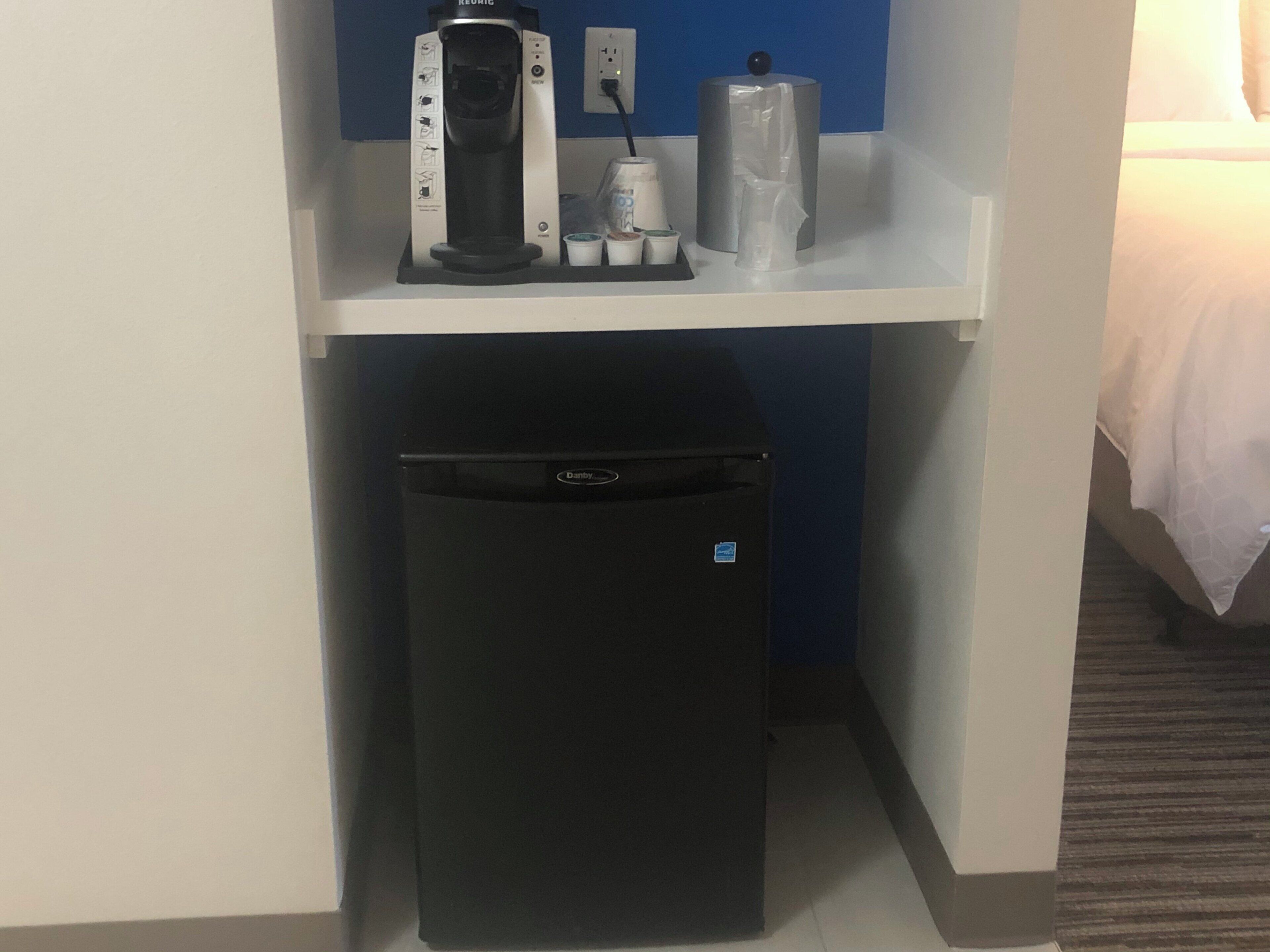 A compact minibar with a coffee maker, a bottle of water, and a small refrigerator.