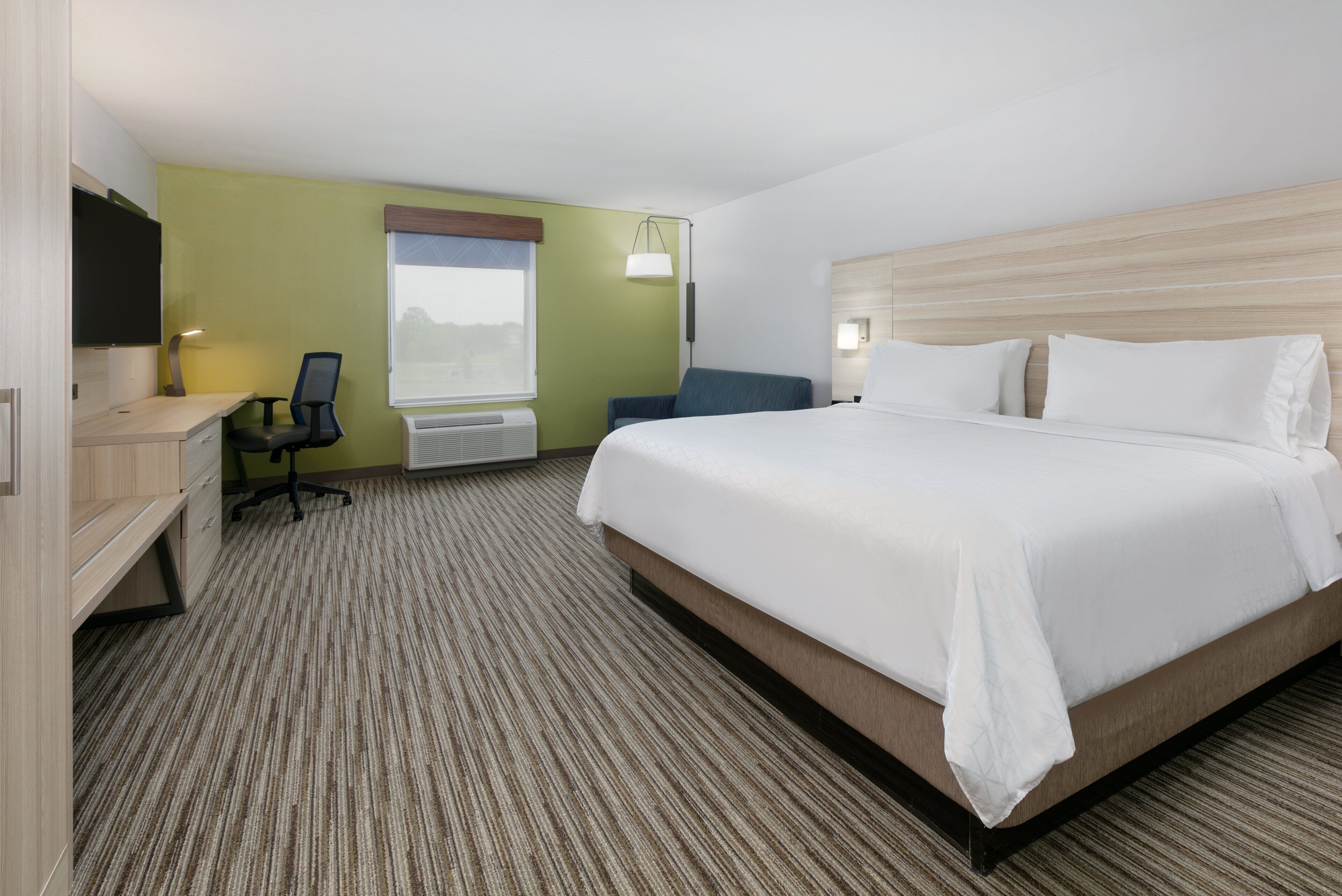 A hotel room with a large bed, a desk with a chair, a television, and a window with a view.