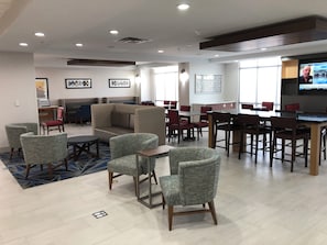 A hotel lobby with a seating area, tables, and a television screen. - Holiday Inn Express : Hillsboro I-35 by IHG (Hillsboro)