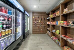 Interior de loja com prateleiras cheias de lanches e uma vitrine refrigerada para bebidas.