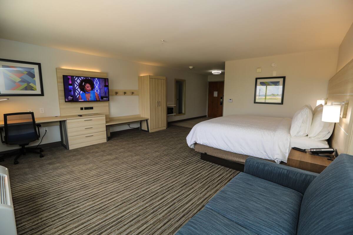 Quarto de hotel com cama, escrivaninha, cadeira, televisão e sofá.