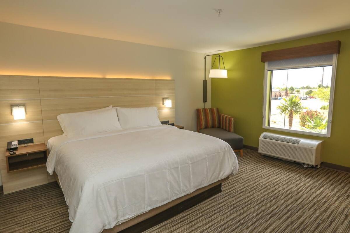 Een hotelkamer met een groot bed, nachtkastjes, een lamp, een raam met uitzicht en een radiator.
