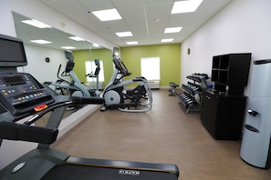 Un gimnasio con equipo cardiovascular, una banca de pesas y una televisión.