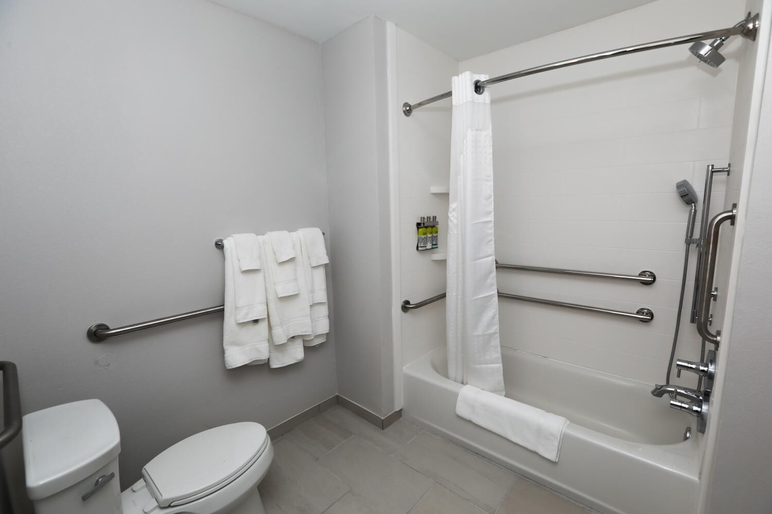 A bathroom with a toilet, a bathtub with grab bars, and a shower curtain.