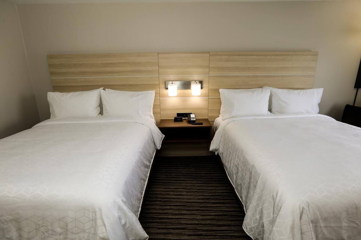 Een hotelkamer met twee bedden, een houten hoofdbord, een nachtkastje met een telefoon en een wandlamp.