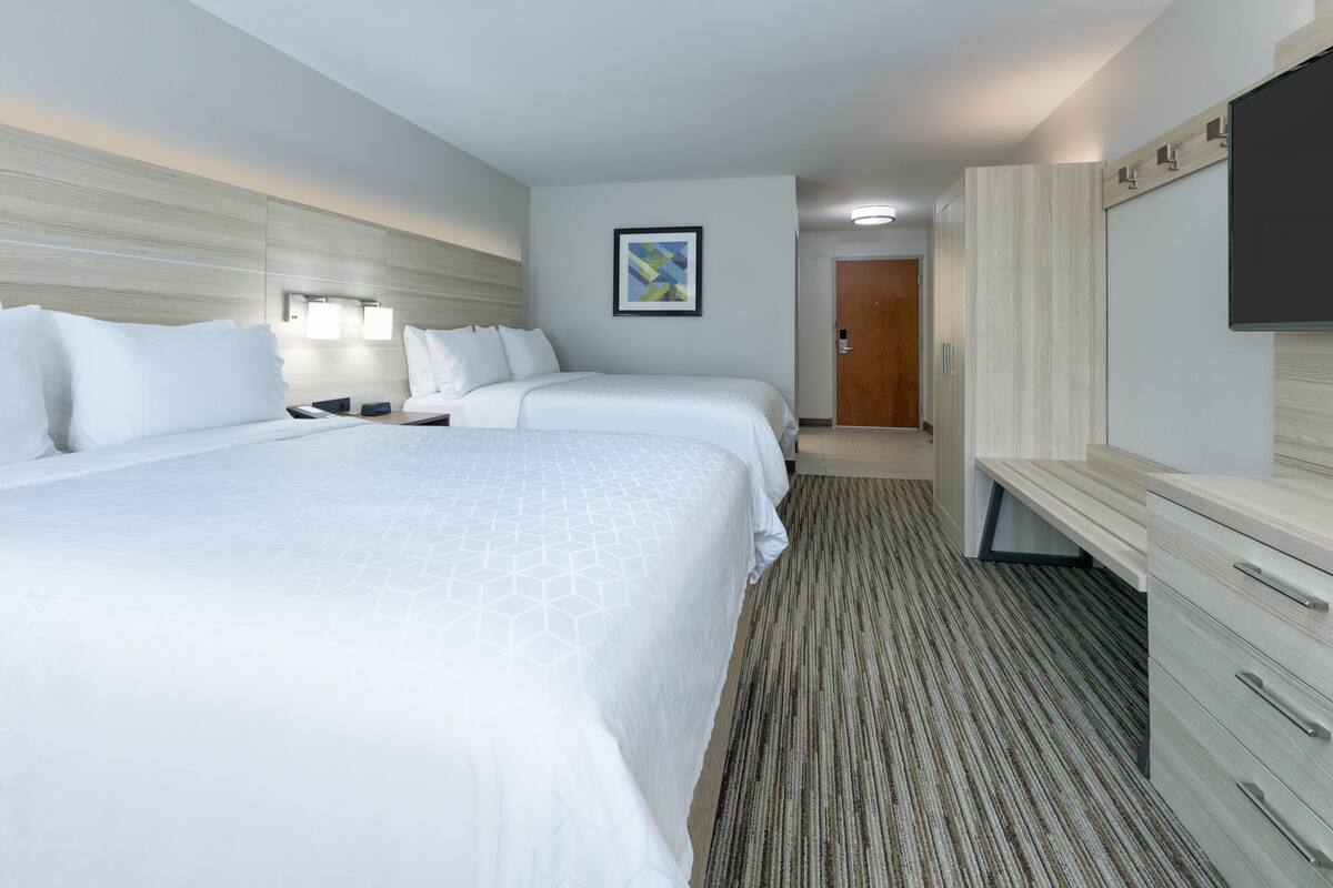 Quarto de hotel com duas camas, uma escrivaninha, um guarda-roupa e um quadro na parede.