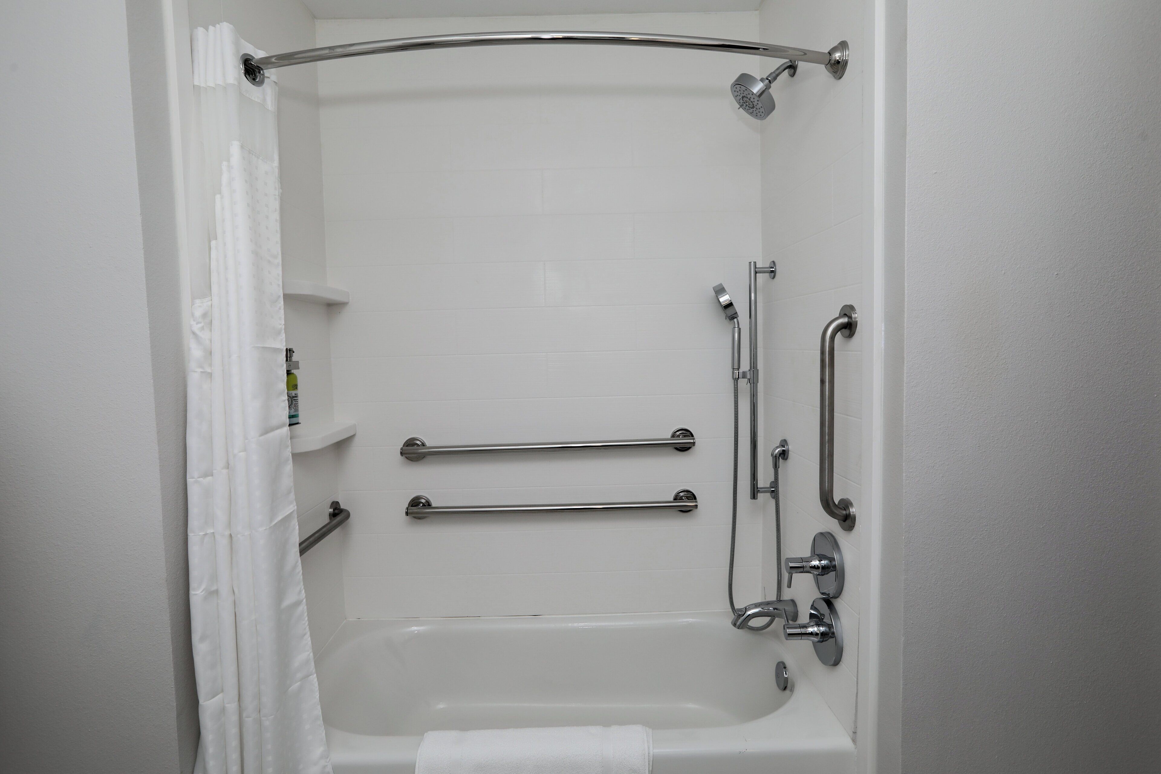 A white bathroom with a bathtub, grab bars, and a shower head.