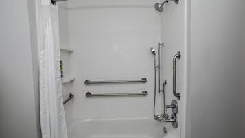 A white bathroom with a bathtub, grab bars, and a shower head.