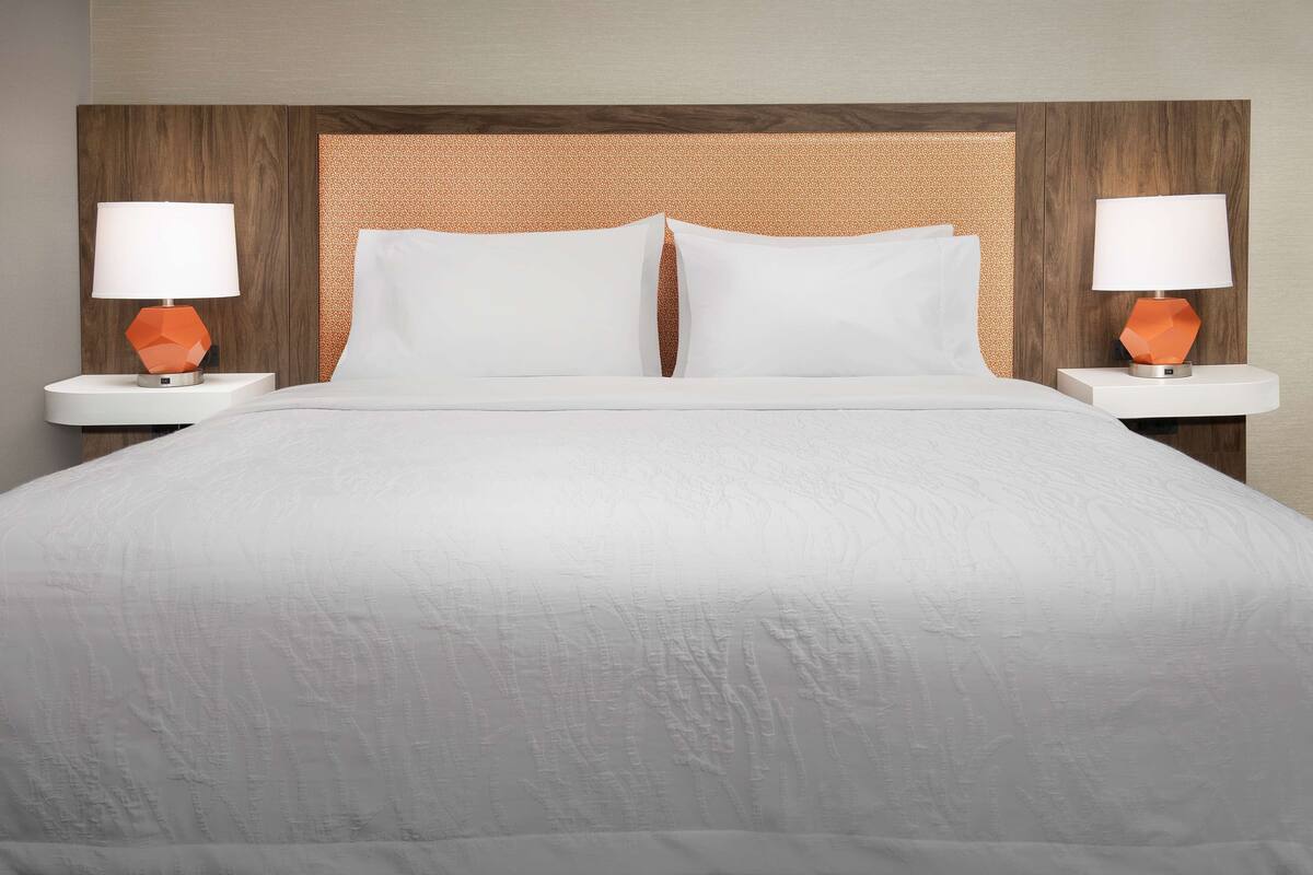 Un lit bien fait, avec du linge de lit blanc et deux tables de chevet surmontées de lampes orange.