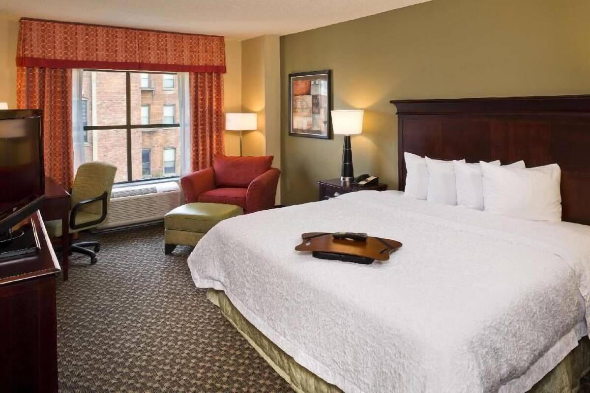 Une chambre d’hôtel avec un grand lit, un bureau avec un ordinateur, une chaise et une fenêtre avec des rideaux.