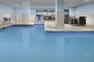 Una piscina con sillas de descanso y una mesa, rodeada de paredes con azulejos y una puerta.