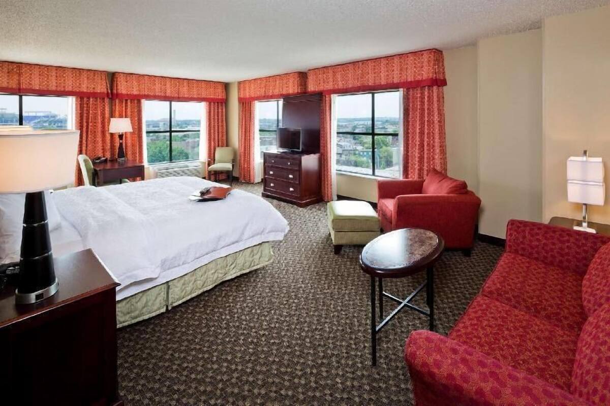 Une chambre d’hôtel avec un lit, un canapé rouge, une petite table, une télévision et une commode.