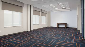 Une chambre d’hôtel spacieuse, dotée d’un tapis à motifs, de grandes fenêtres et d’une petite table en bois.