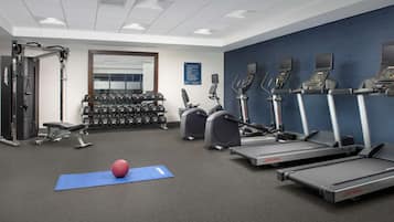 Une salle de sport équipée de tapis de course, de vélos elliptiques, d’haltères et d’un tapis de yoga.