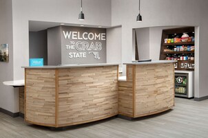 Un mostrador de recepción con un cartel que dice 'Welcome to the Crab State', un mini bar y una estantería con aperitivos.