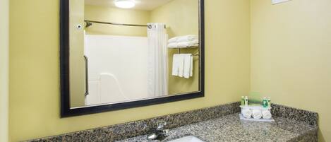 A bathroom with a granite countertop, a sink, a mirror, a towel rack with folded towels, and a sign with toiletries.