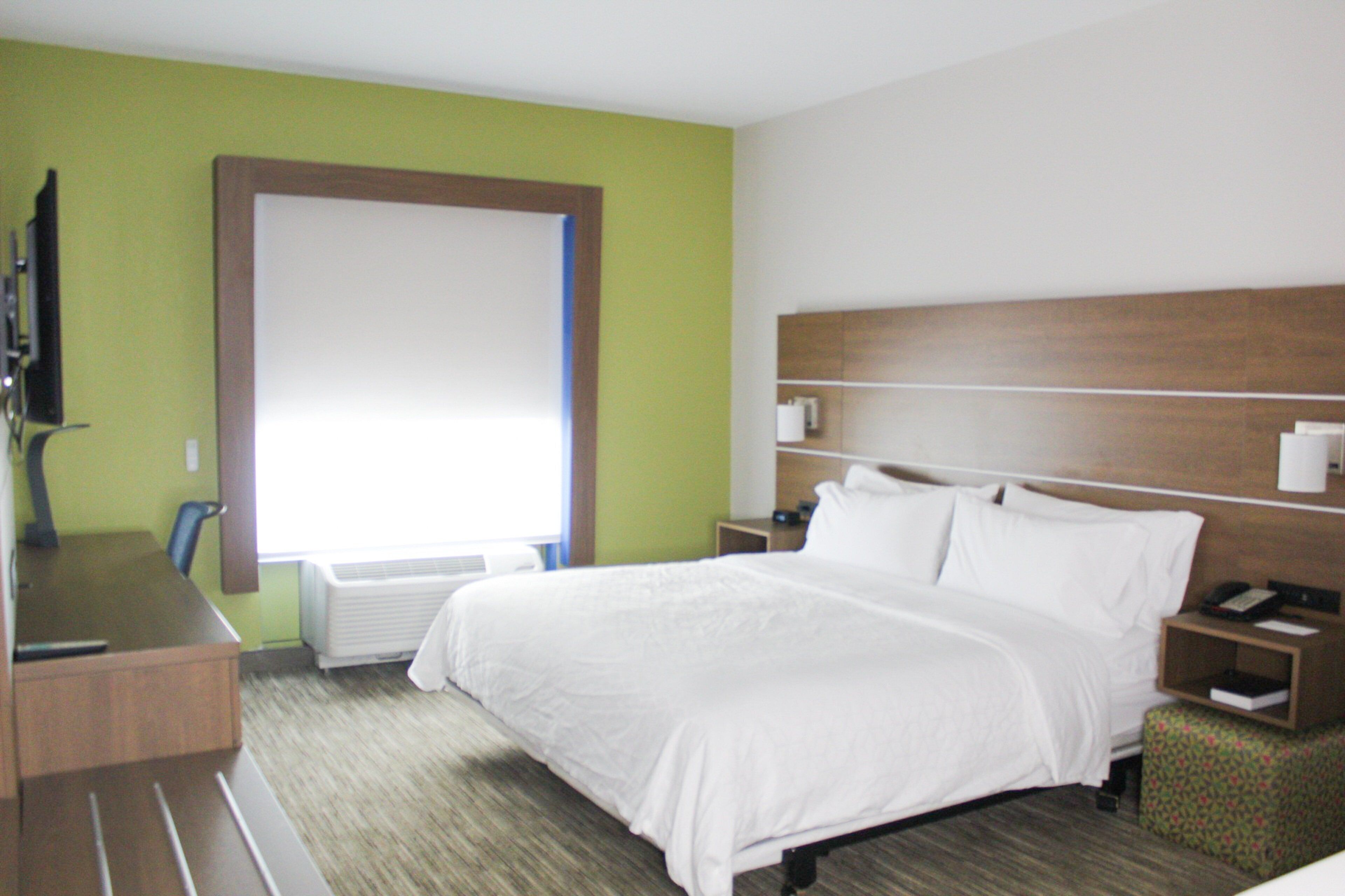 A hotel room with a bed, a desk, a chair, a nightstand, a lamp, and a window.