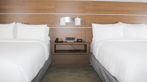 A hotel room with two beds, a wooden headboard, a nightstand with a clock, and a small shelf.