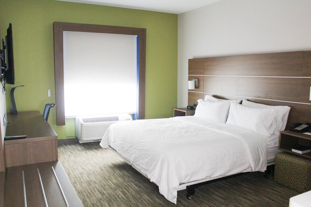 Une chambre d’hôtel avec un lit, un bureau, une chaise, une table de chevet, une lampe et une fenêtre.