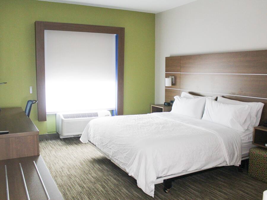 Habitación de hotel con cama, escritorio, silla, mesita de noche, lámpara y ventana.