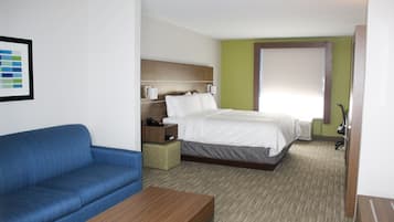 A hotel room with a bed, a blue sofa, a wooden table, and a small bedside table with a lamp.
