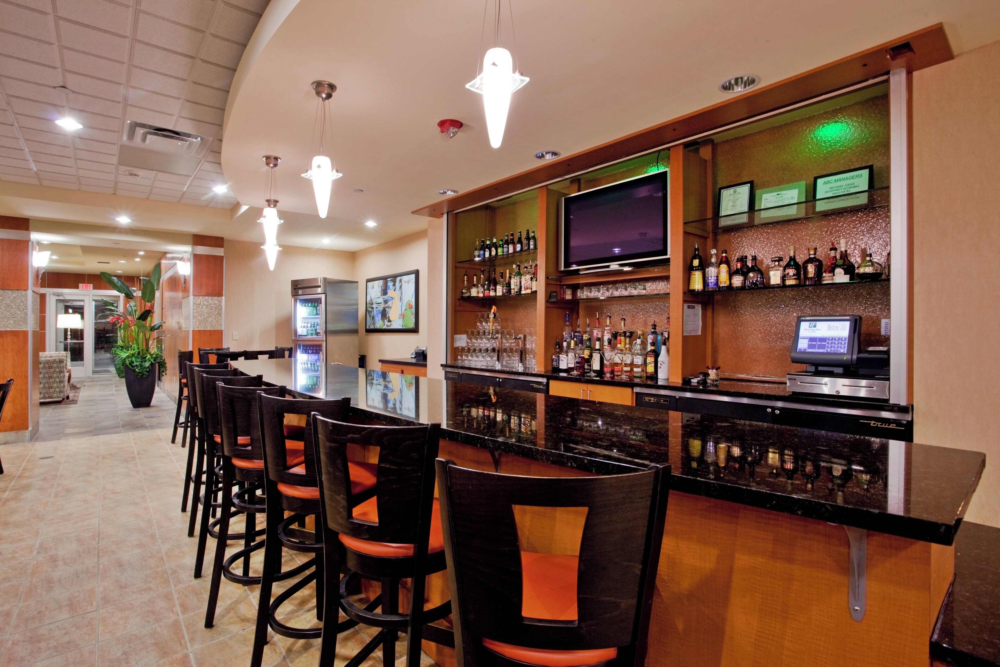 A bar area with a long counter, multiple chairs, a television, and a variety of bottles and glasses.