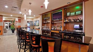A bar area with a long counter, multiple chairs, a television, and a variety of bottles and glasses.