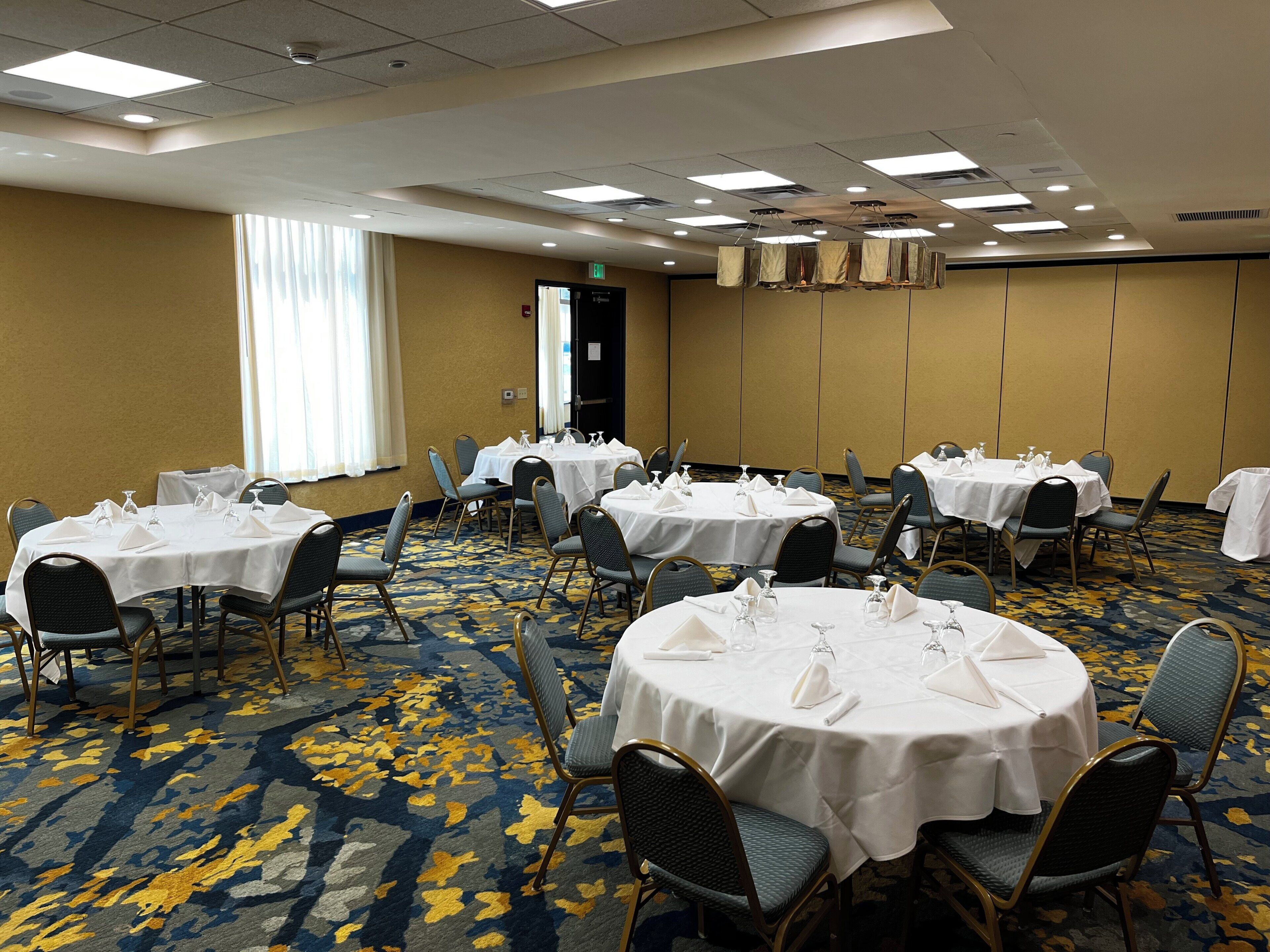 A conference room with multiple round tables, chairs, and a carpeted floor.