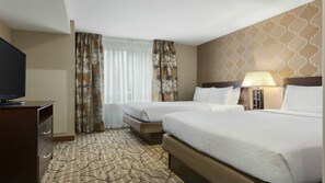 Ein Hotelzimmer mit zwei Betten, einem Fernseher, einem Schreibtisch und einem gemusterten Teppich.