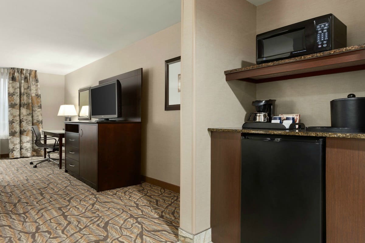 Een hotelkamer met een bed, een bureau met stoel, een televisie, een magnetron, een koffiezetapparaat en een koelkast.