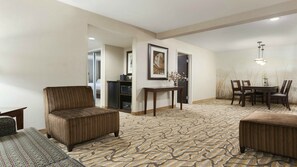 Ein Hotelzimmer mit einem gemusterten Teppich, einer Couch, einem Esstisch mit Stühlen und einem kleinen Beistelltisch mit Blumen.