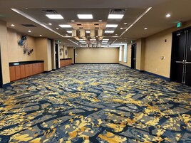 Un vestíbulo de hotel con alfombra estampada, luces de techo y un largo pasillo que conduce a las puertas.