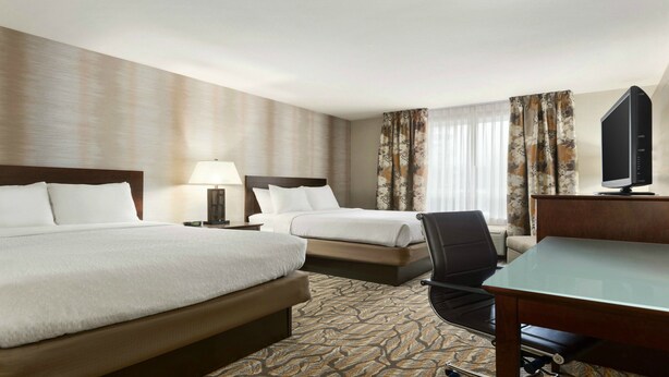 A hotel room with two beds, a desk, a chair, a television, and a clock on the nightstand. - Holiday Inn Hotel & Suites Williamsburg-Historic Gateway by IHG (Williamsburg)