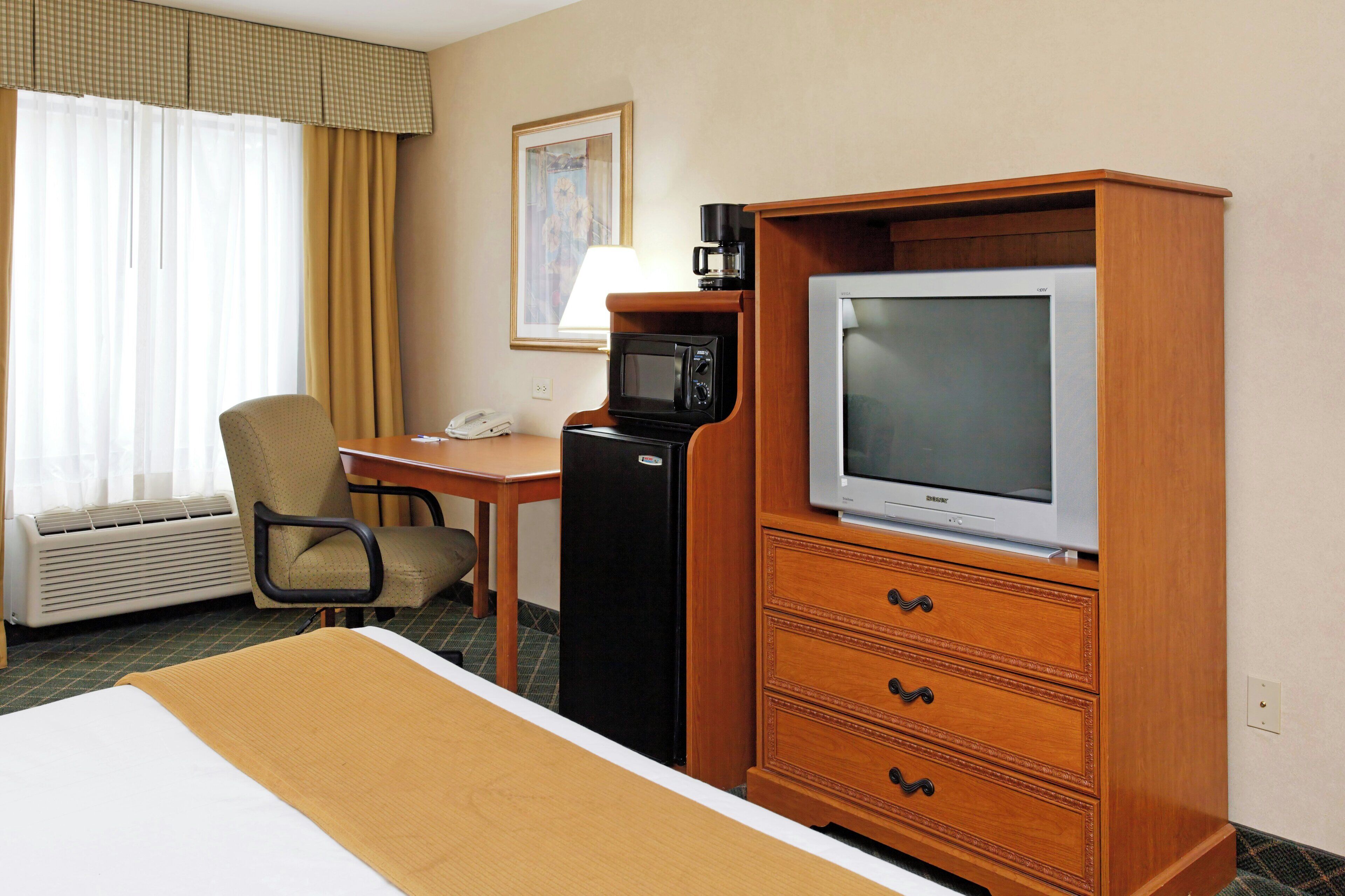 Habitación de hotel con cama, escritorio, televisor, refrigerador y una silla.
