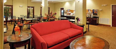 A hotel lobby with a red sofa, dining tables, chairs, a coffee station, and a large window.